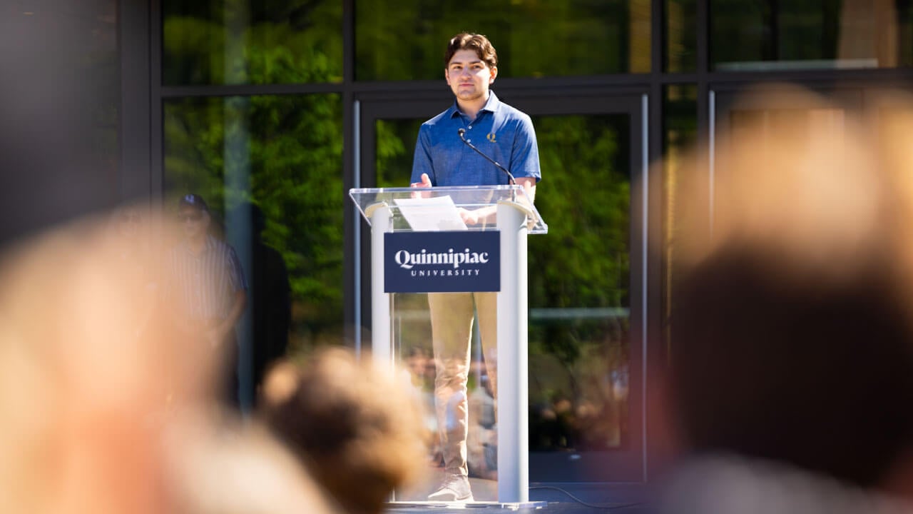 Student stands at podium speaking to a crowd