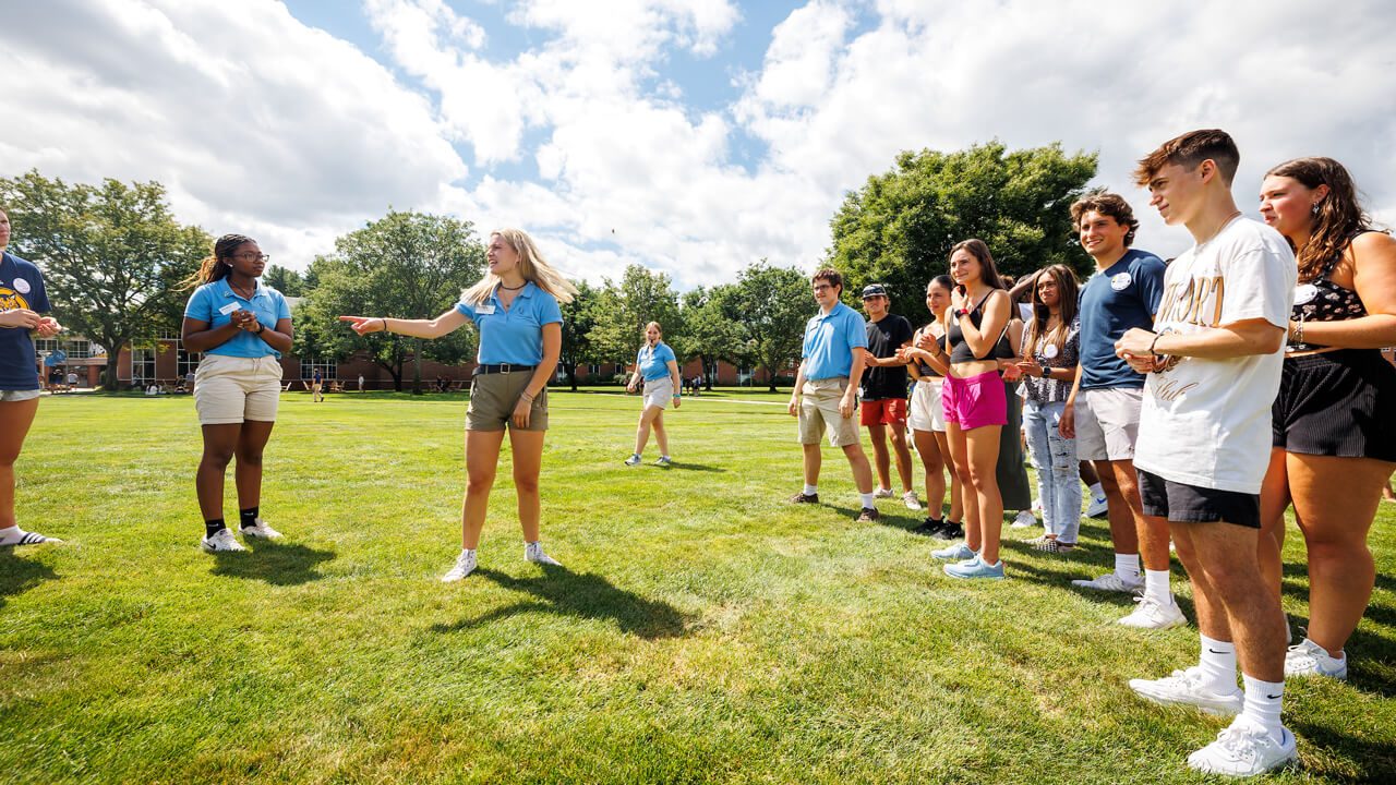 A group of new students and orientation leaders play an ice breaker game in the grass