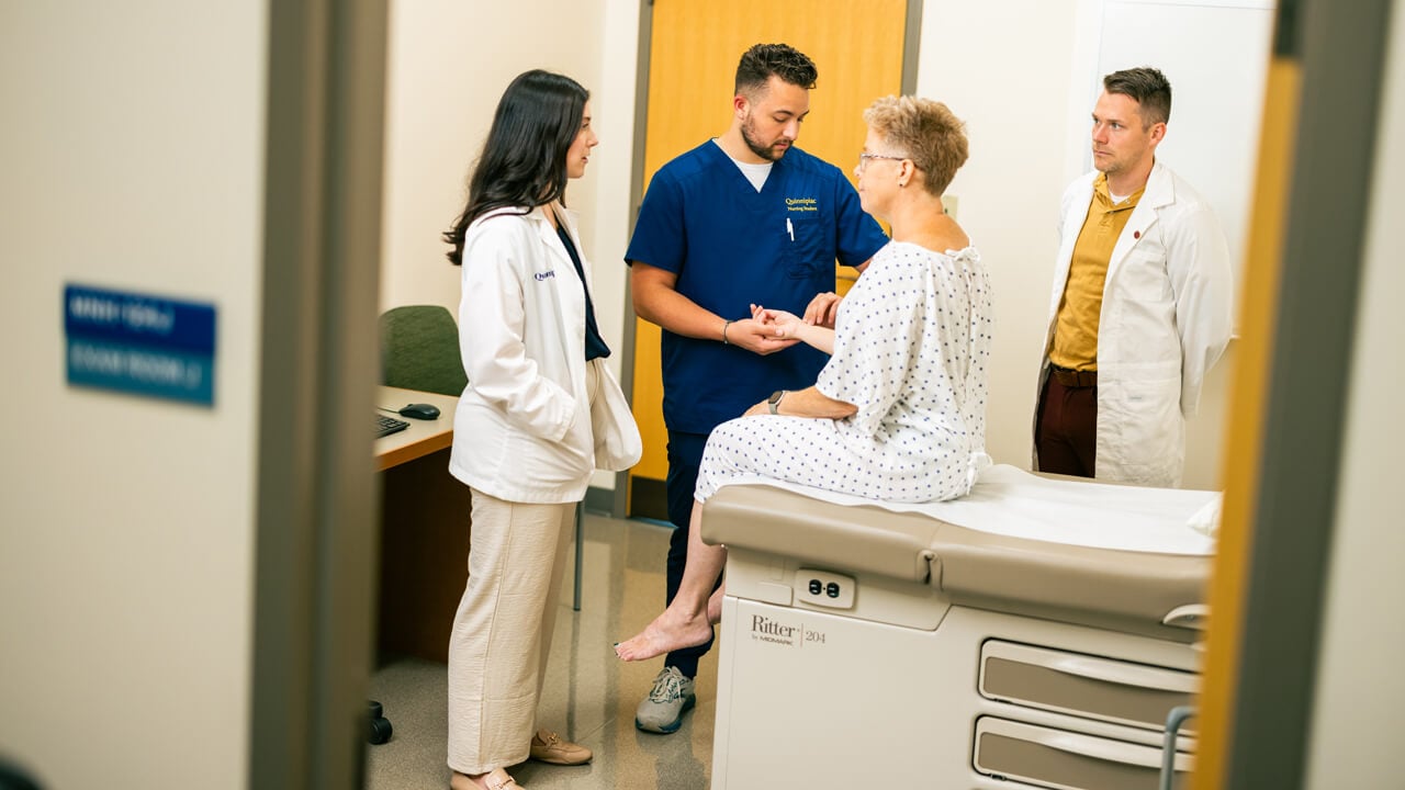 Two nursing students receive faculty direction while performing an exam on a standardized patient.