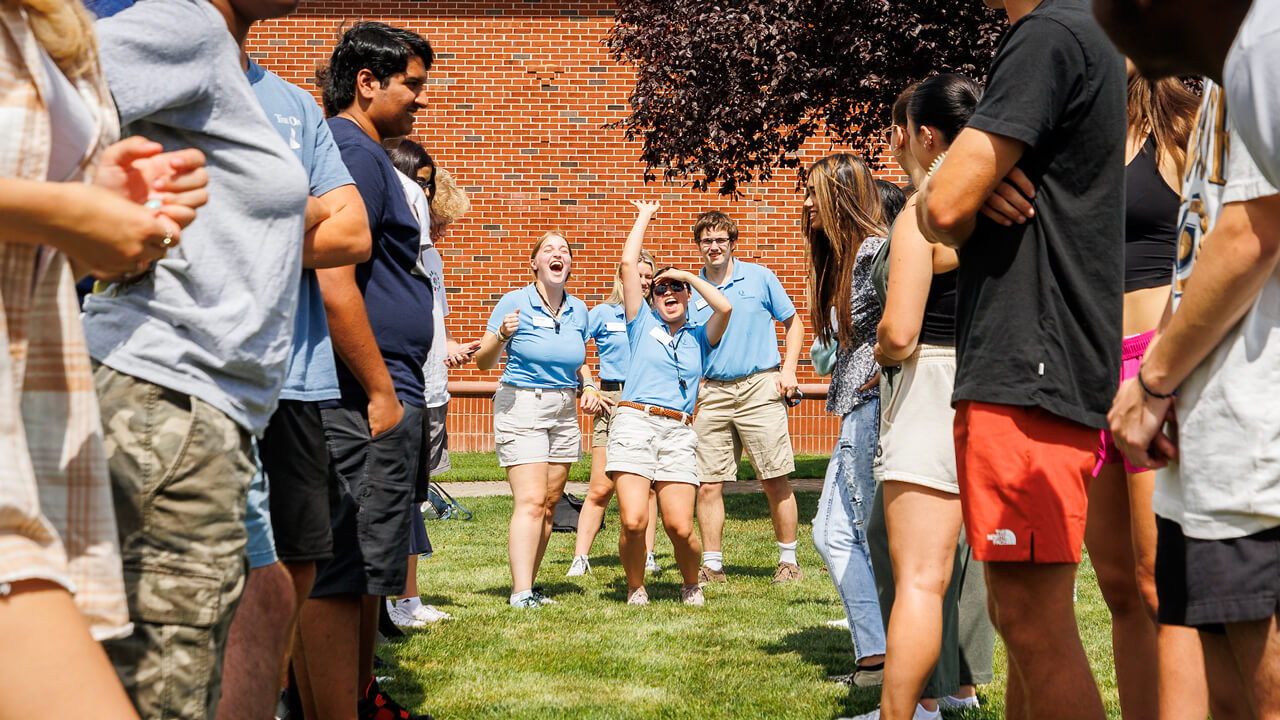 Four orientation leaders cheer enthusiastically among a group of new students