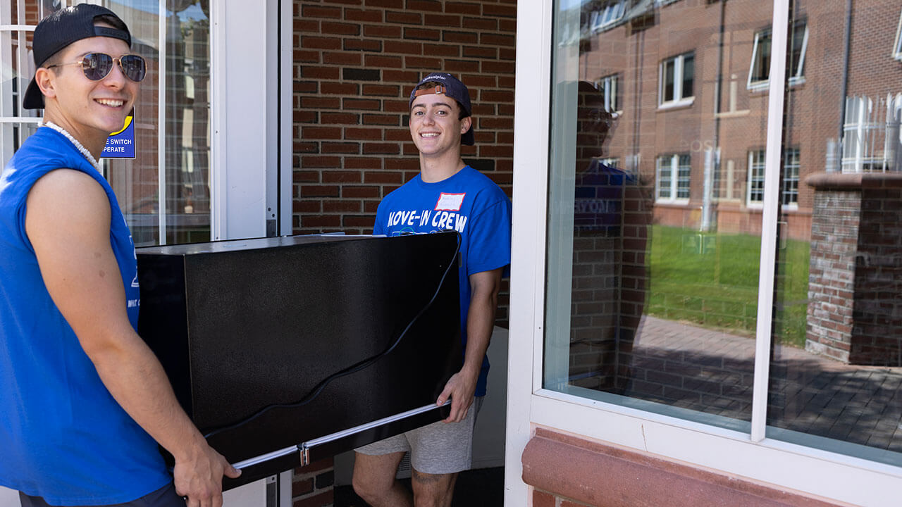 Two students carry a refrigerator into a residence hall