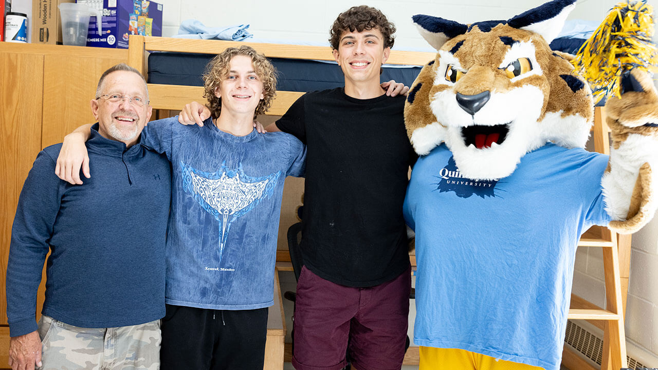 A family with two new students take a photo with Boomer in their dorm