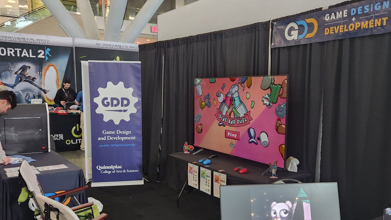 Quinnipiac's Game Design and Development booth at Pax East, with chairs in front of a monitor.