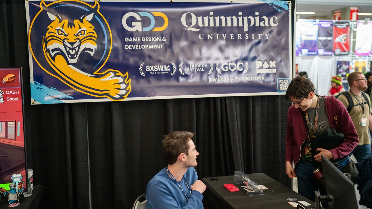 A participant looking at the Game Design & Development booth below a banner showing the growler and the program's various award wins.