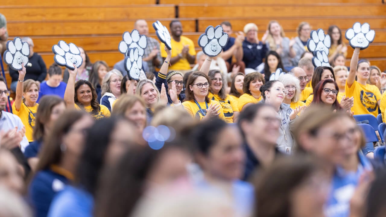 Health sciences faculty and staff in matching gold tee shirts cheer and wave foam Bobcat paws