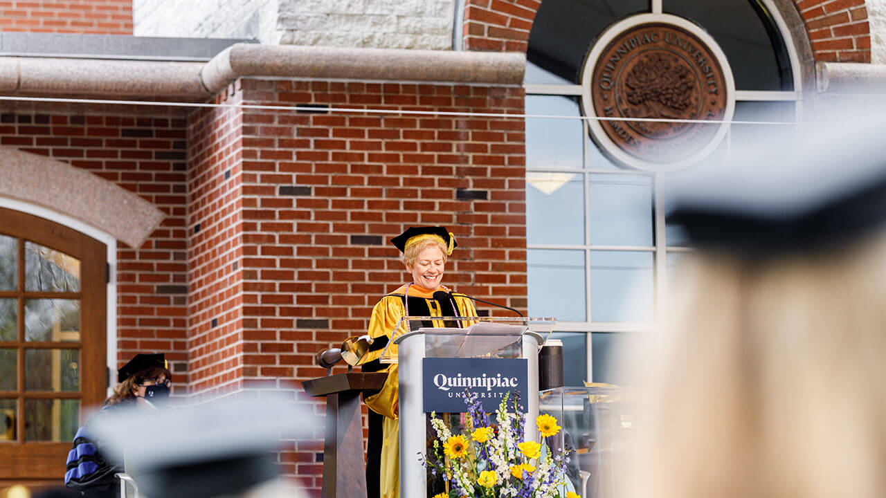 Beth Beckman speaks from the podium on the library steps during Commencement