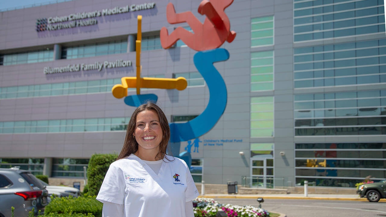 Jillian Isolano wears scrubs and smiles outside the Cohen Children’s Medical Center