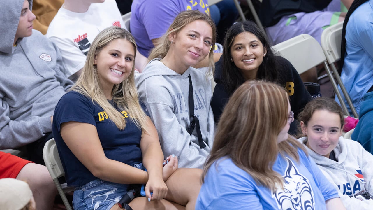 Three students sit together and smile arm in arm during the welcome ceremony