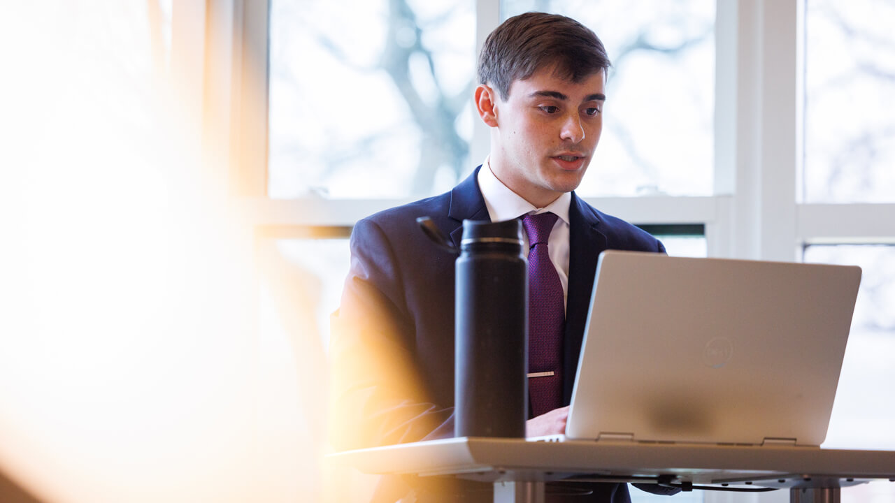 Student in a suit sitting with his laptop