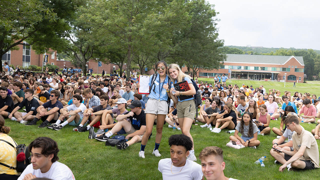 Two orientation leaders cheer as they stand among hundreds of new students on the quad