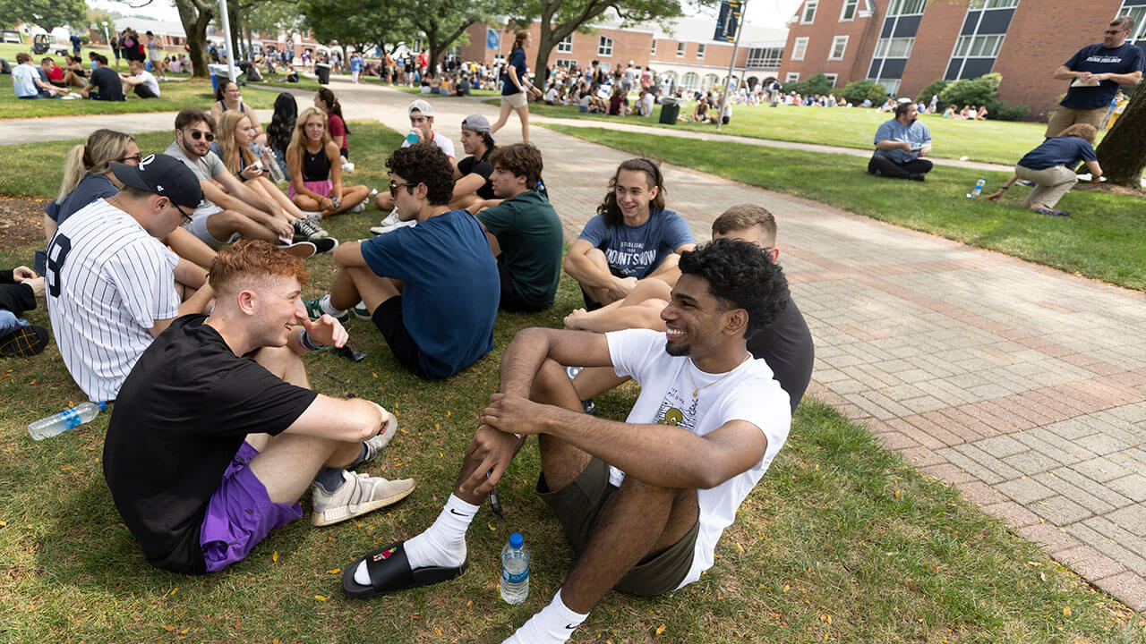 Hundreds of students sit in small groups on the quad grass