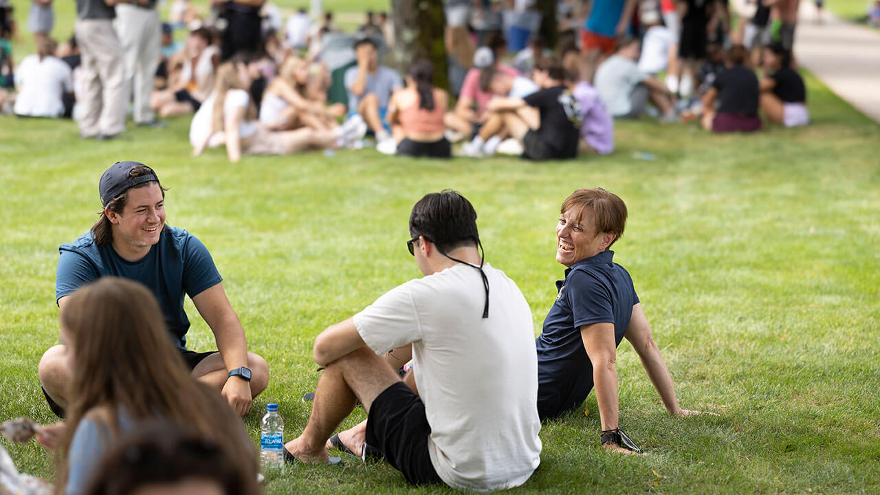 Students sit with a faculty member on the grass on the quad