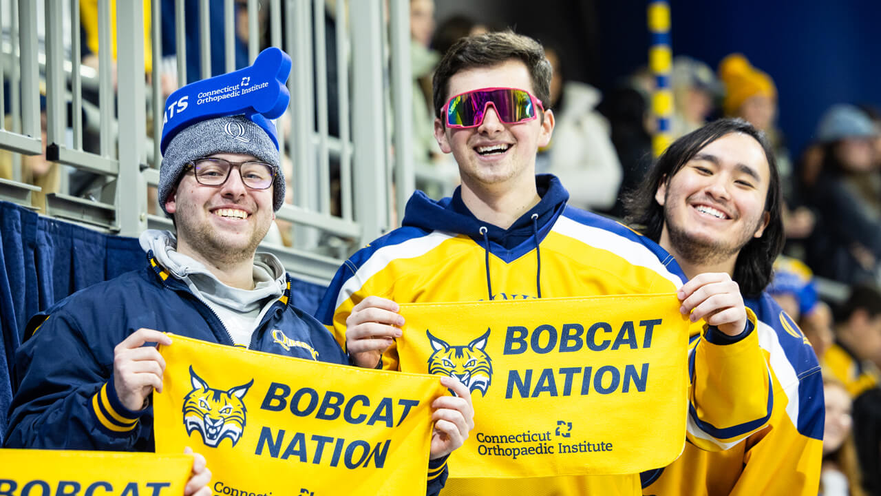 Three Bobcats fans in hockey jerseys hold up Bobcat Nation rally towels in the hockey stadium