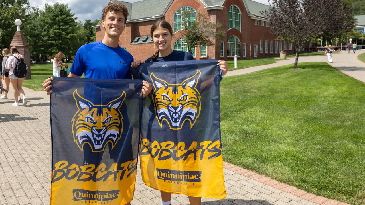 Students smile for camera holding Quinnipiac flags