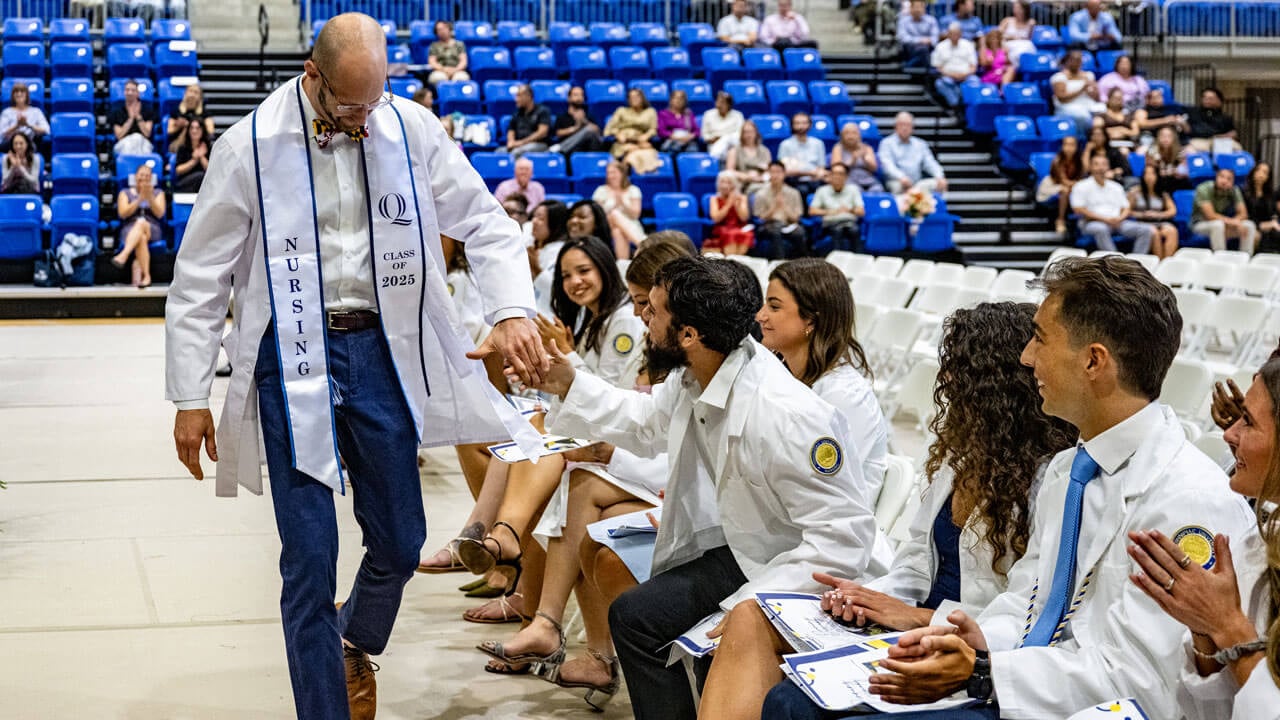 Students in white coats sitting down at the 2025 pinning ceremony