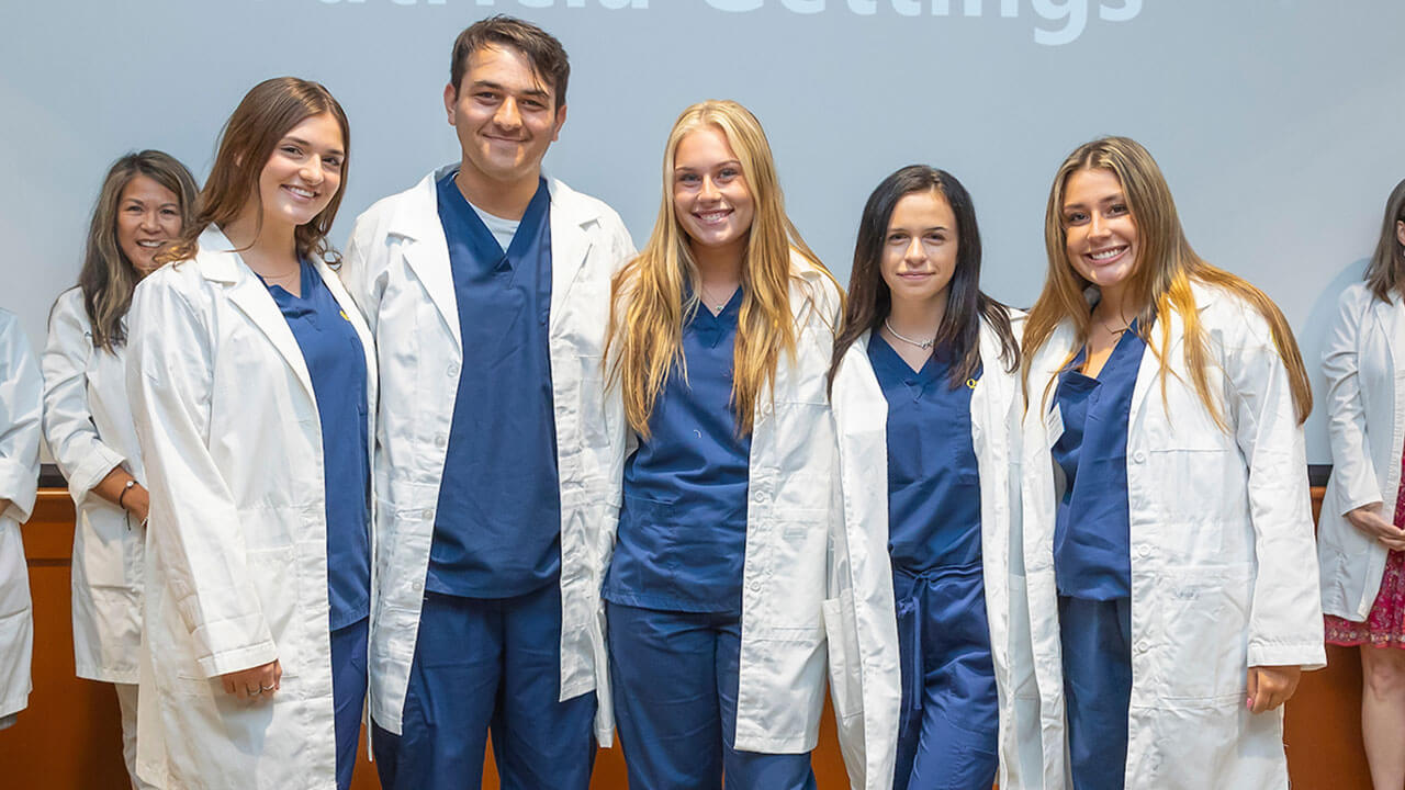 five nursing students wear their new white coats to take a photo together