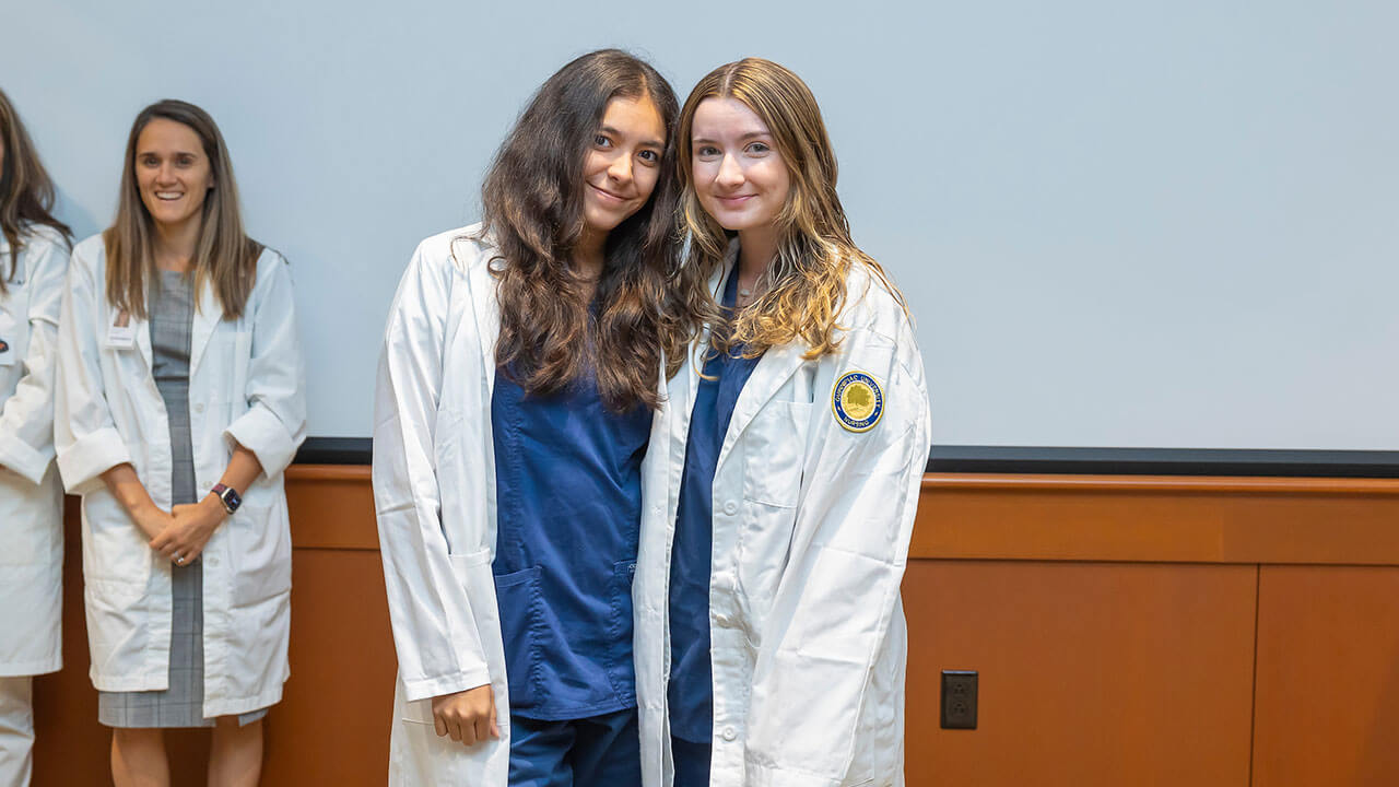 two nursing students pose together showing off their new white coats