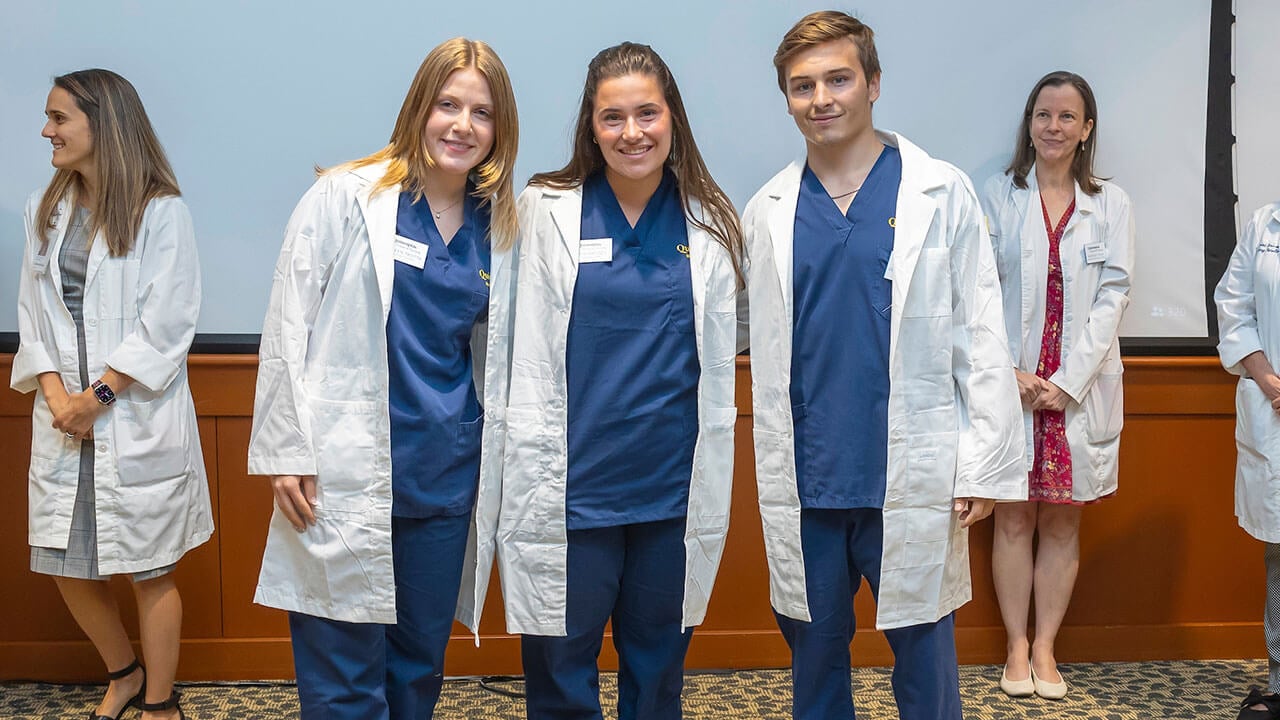 three nursing students pose smiling in their new white coats