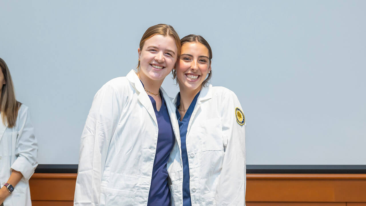 two nursing student smile excitedly in their new white coats
