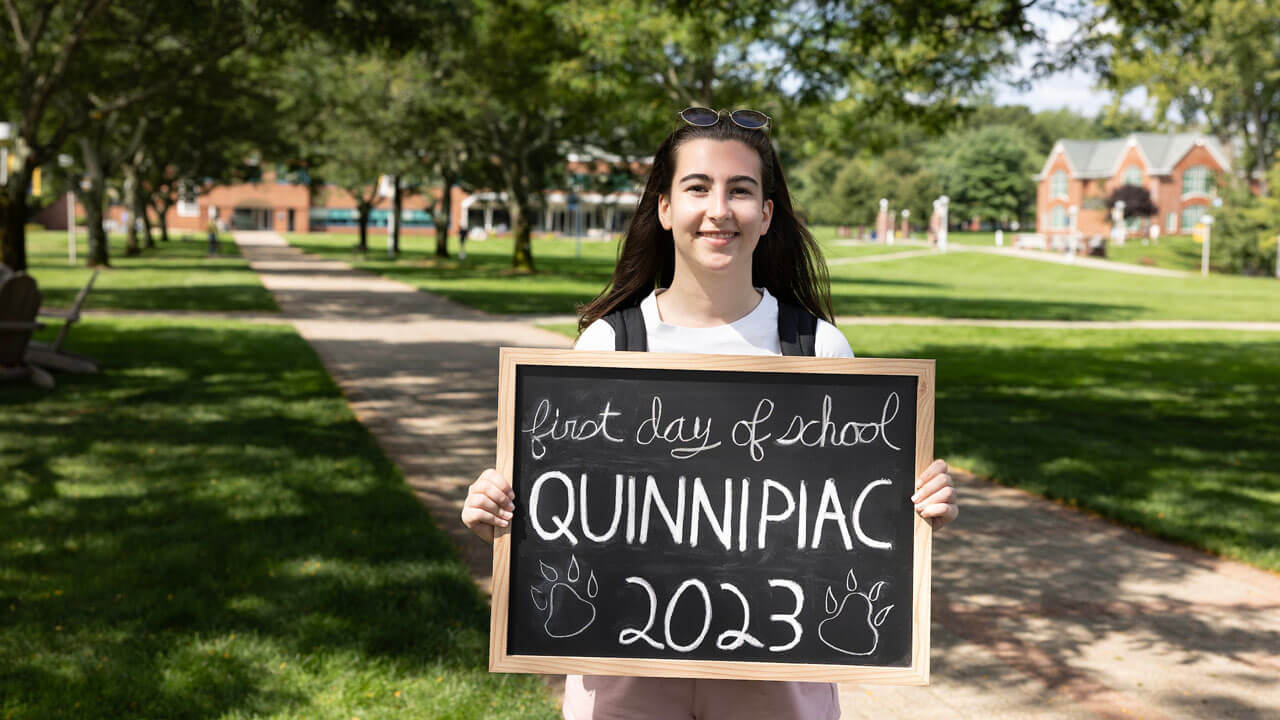 Student poses for a photo with a first day of school sign