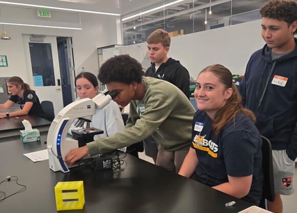 A group of students working around a microscope at a lab table.