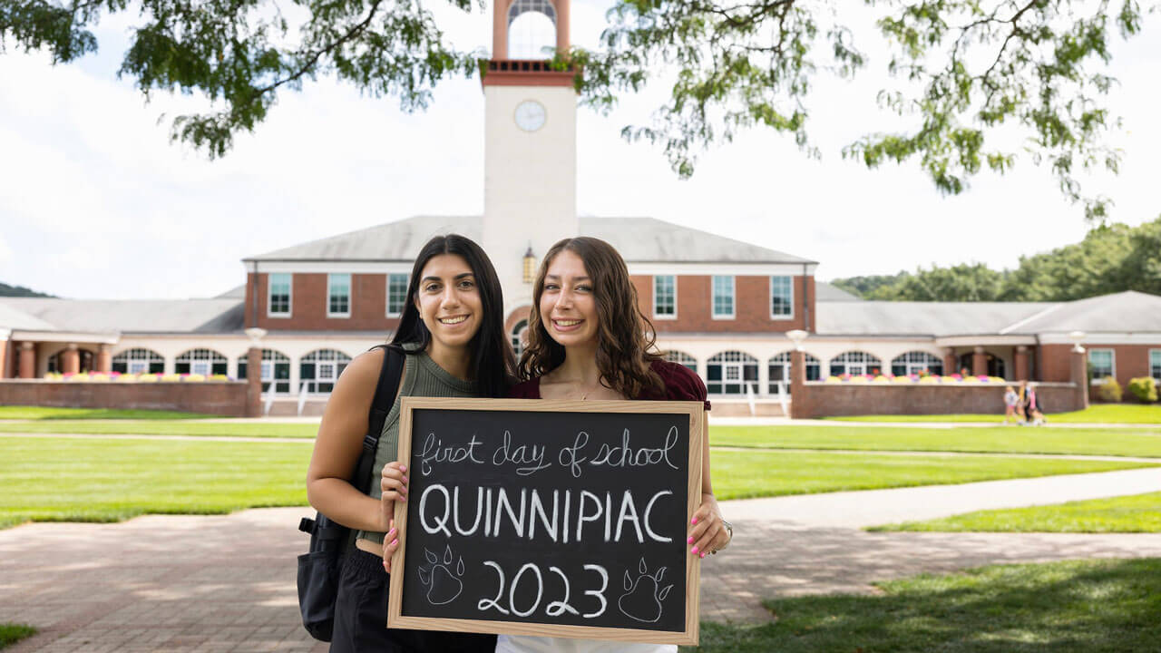 Two students smile with a sign