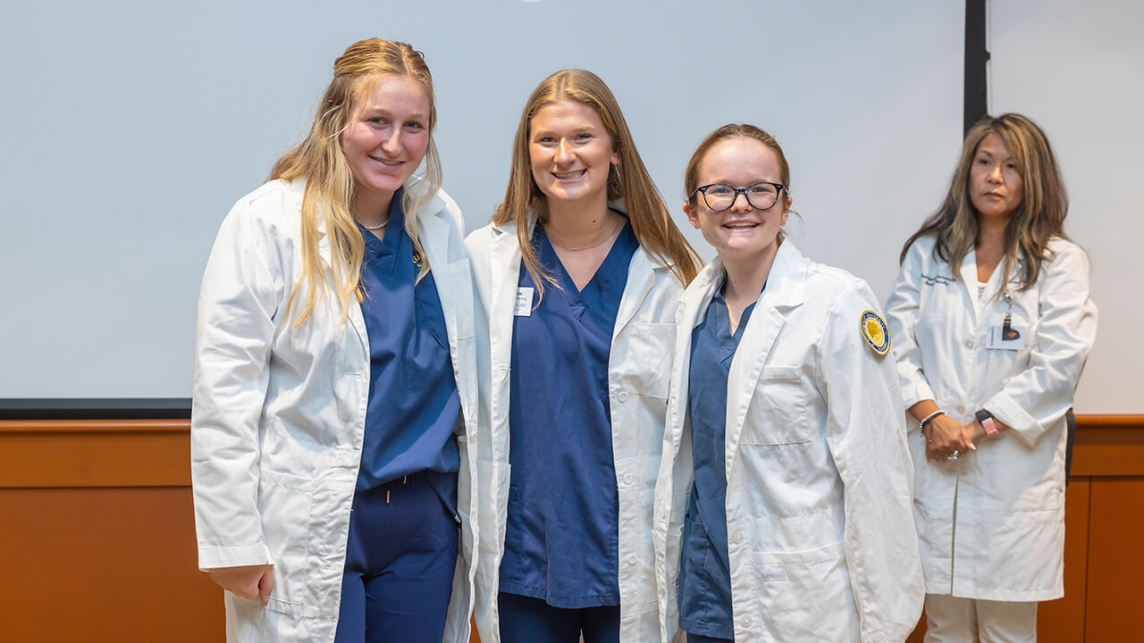 three nursing students pose wearing their white coats