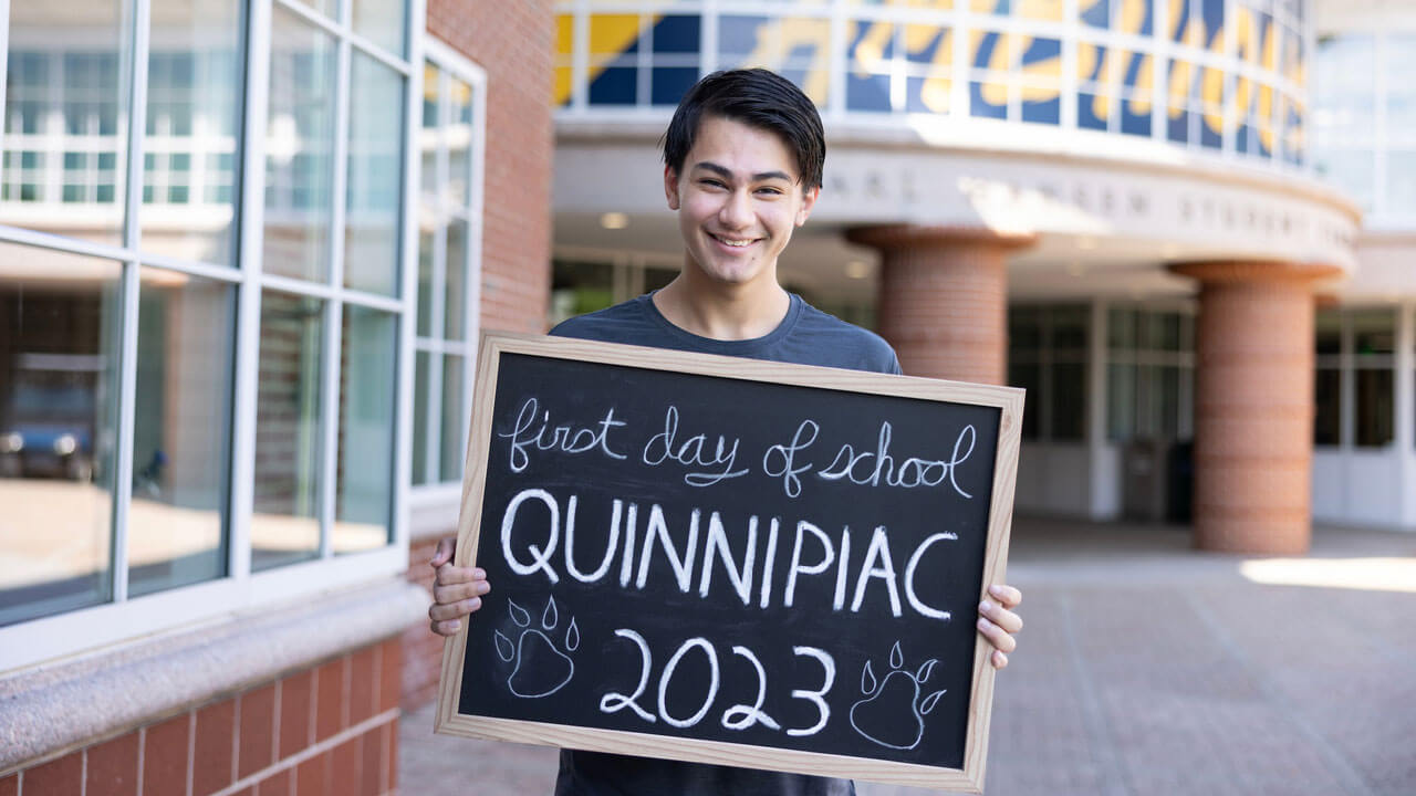 A student smiles with a sign in front of the Student Center