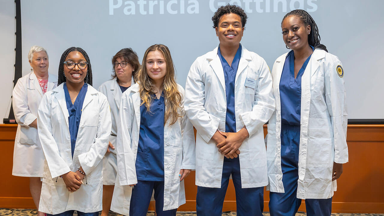 four nursing students in white coats pose for a photo