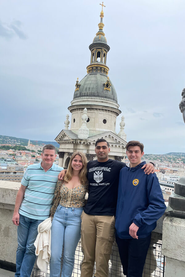 Prof Chris Ball with 3 student in front of Budapest skyline