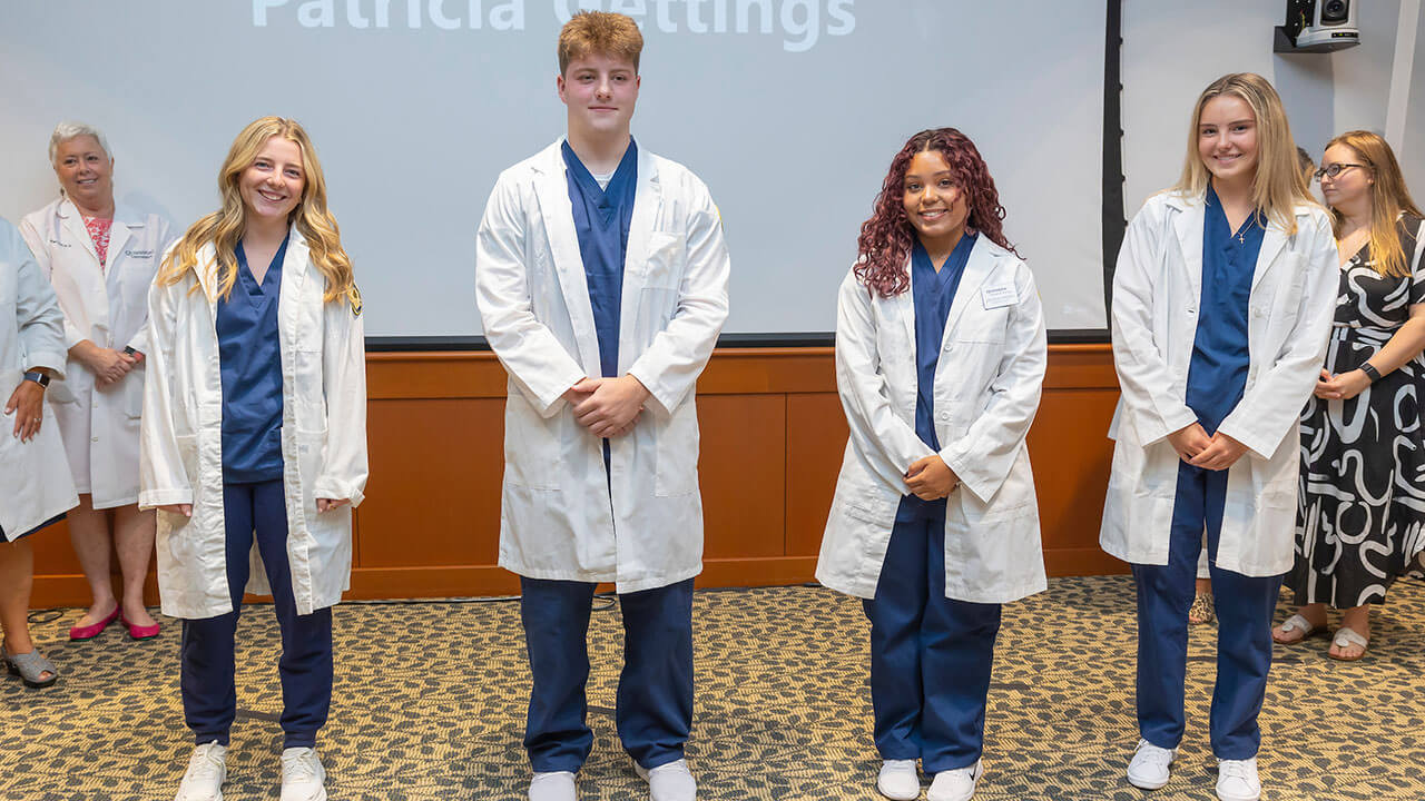 four nursing students pose for their photo to be taken in their white coats