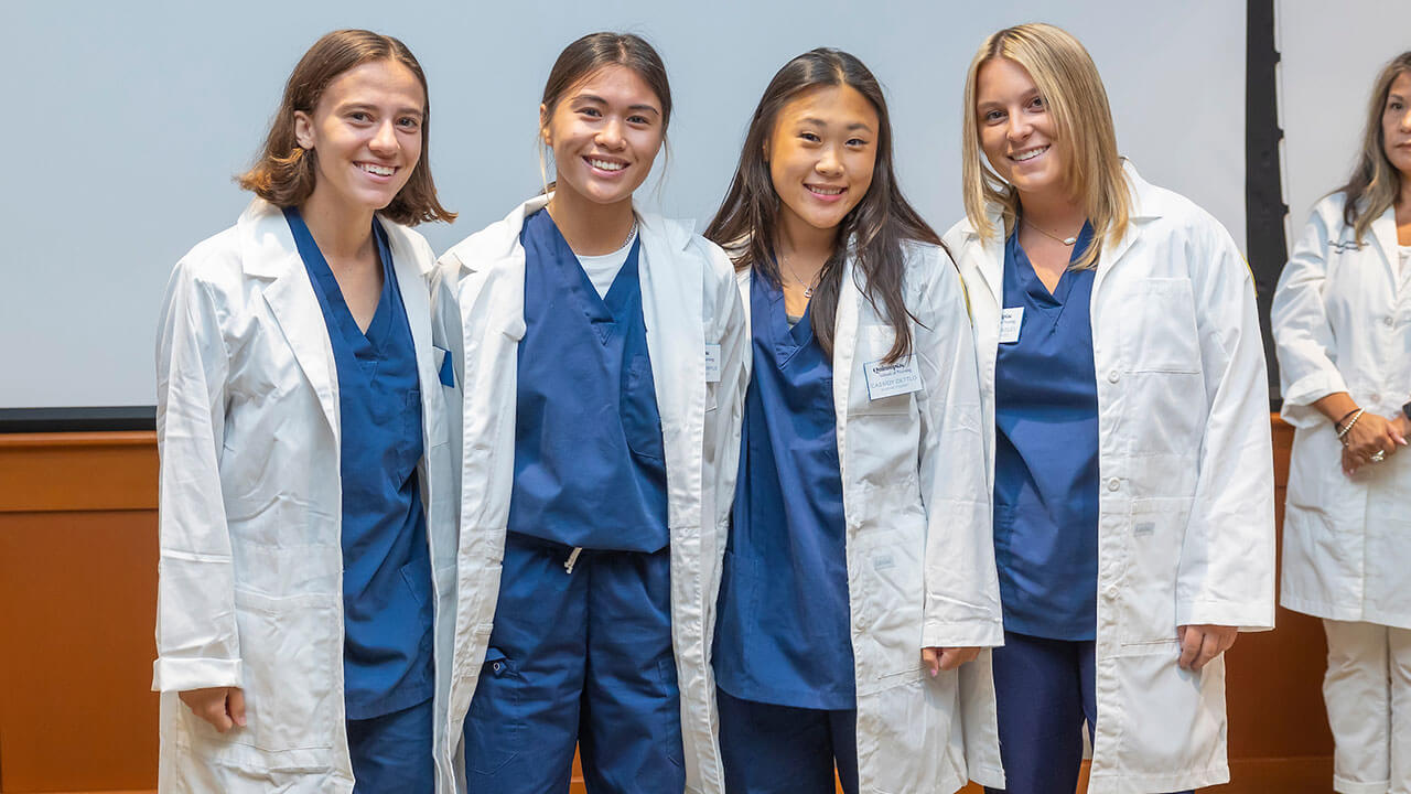 four nursing students in white coats pose for their photo to be taken