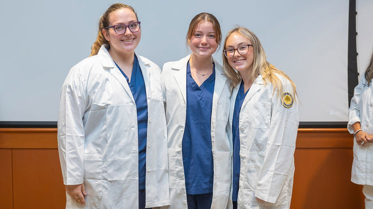 three nursing students smile in their white coats