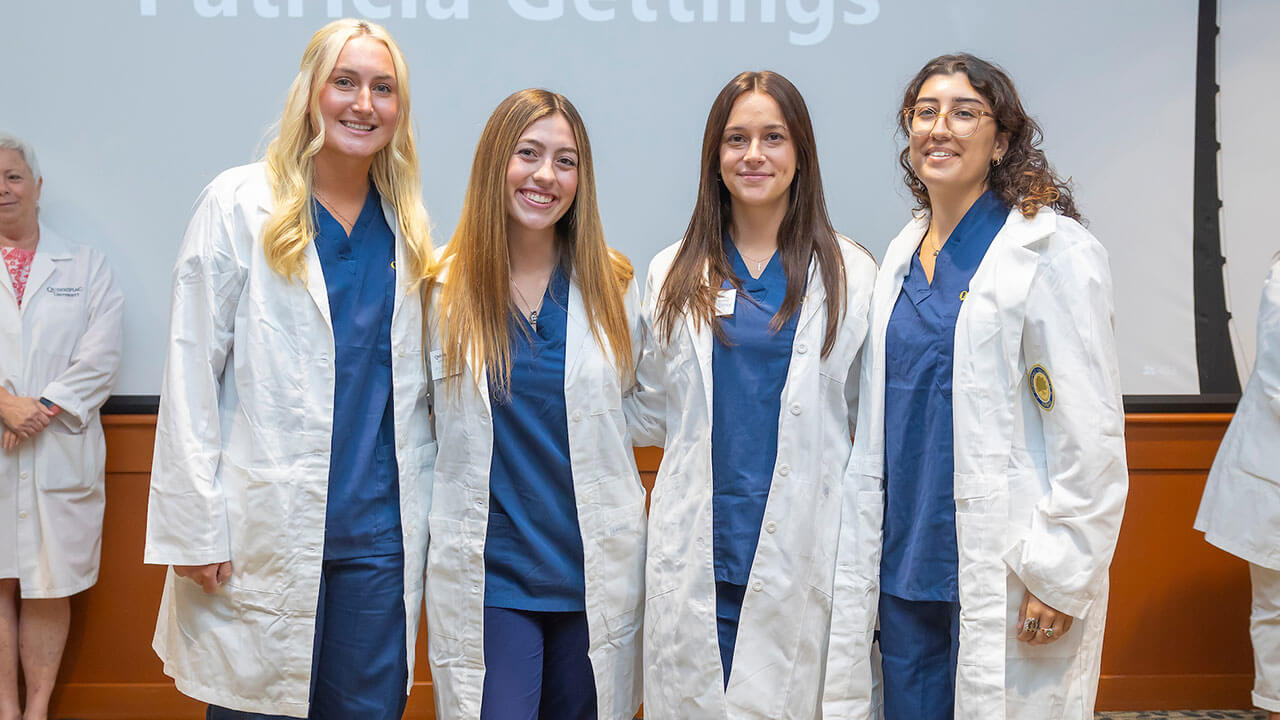 four nursing students in white coats pose for their photo to be taken