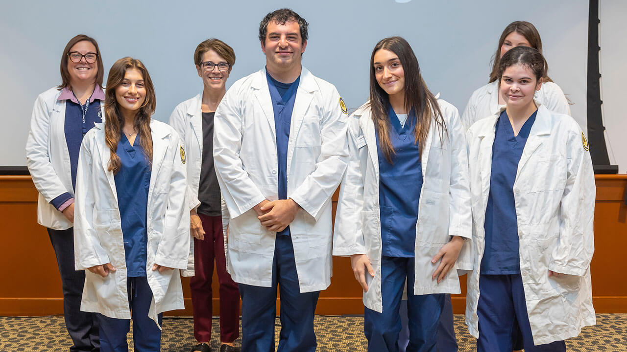 four nursing students in white coats pose for their photo