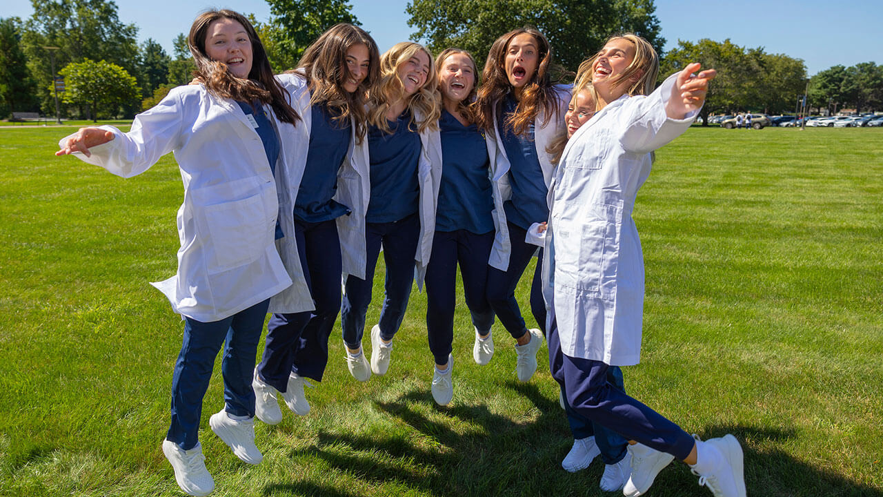 six nursing students jump in the air wearing their white coats
