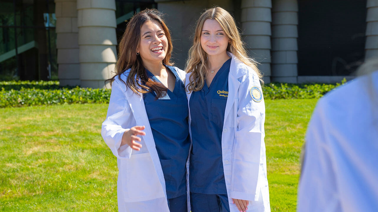 two nursing students in white coats have their photo taken outside