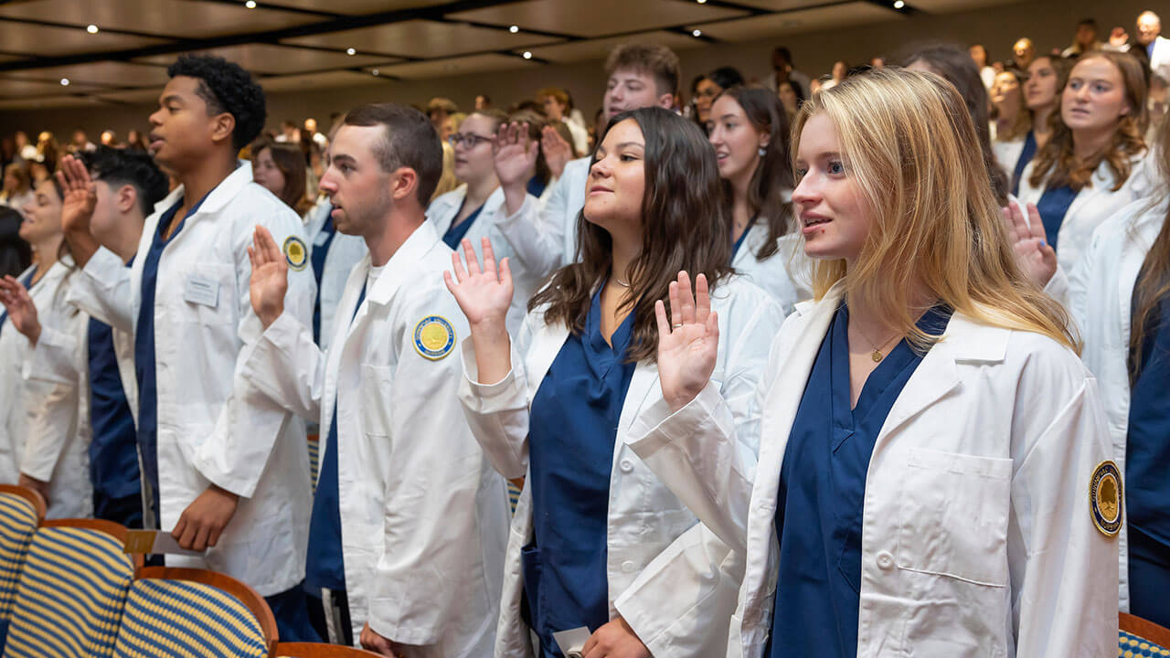 rows of nursing students raise their right hands to take an oath