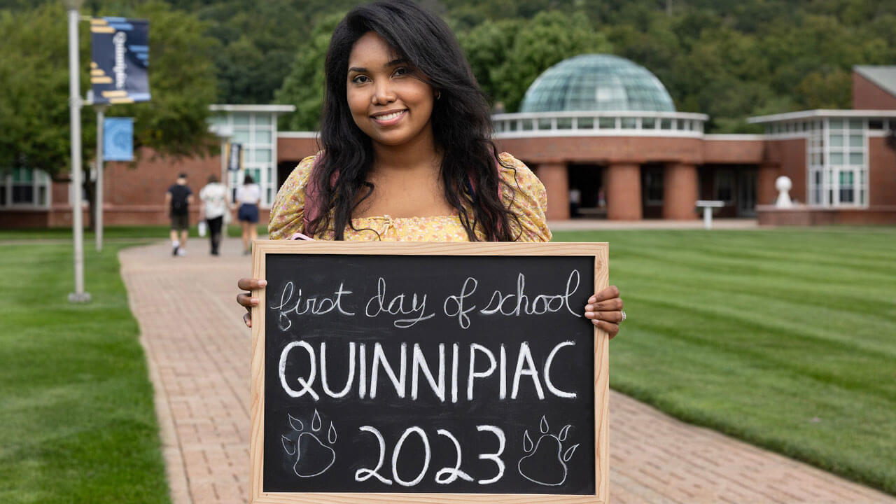 Student holding first day of classes chalkboard in front of the school of business building