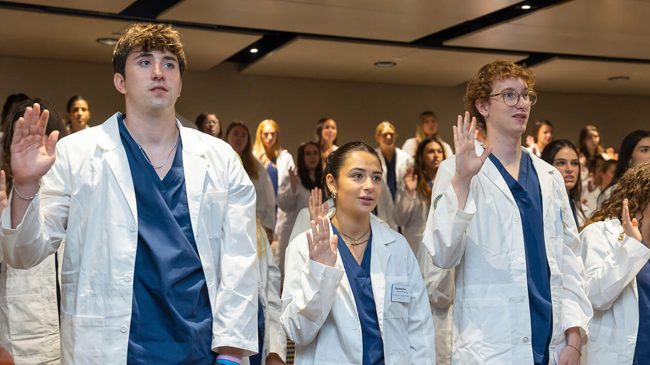 rows of nursing students in white coats prepare to take an oath