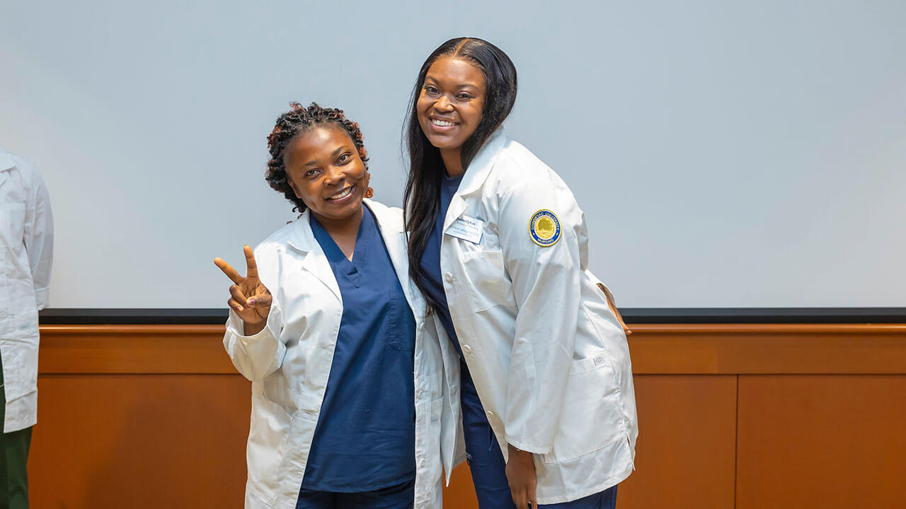 two nursing students wearing white coats pose for their photo to be taken