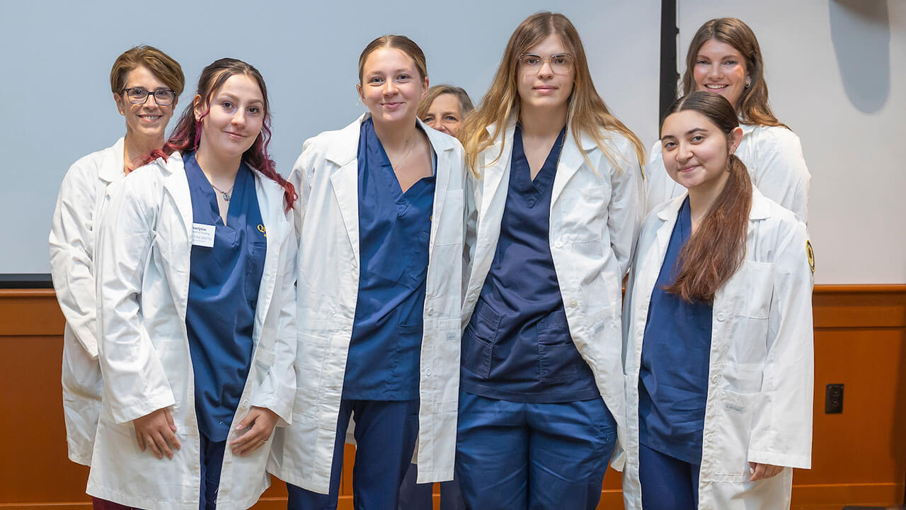 four nursing students wear white coats and pose for their photo to be taken