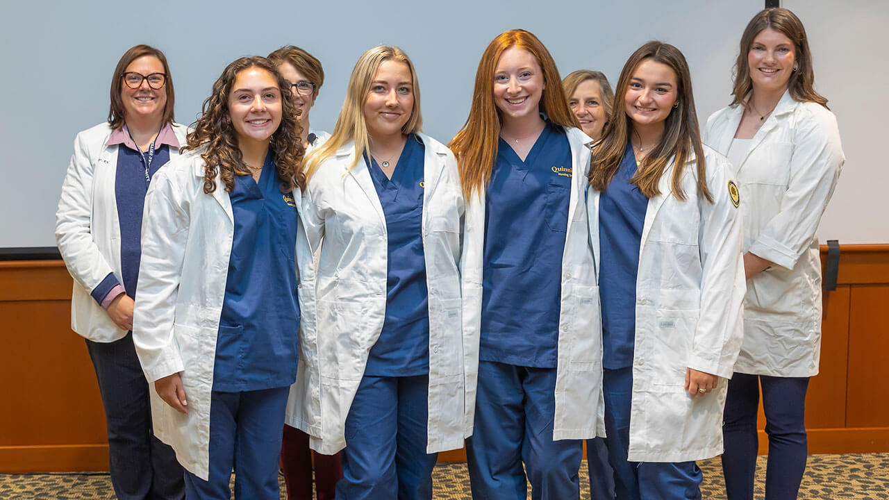 four nursing students smile in their white coats