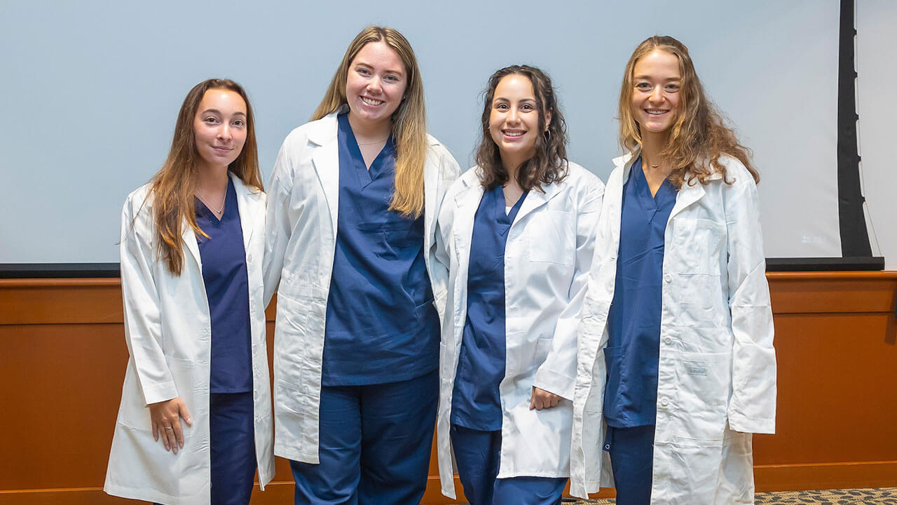four nursing students smile for a photo while wearing their white coats