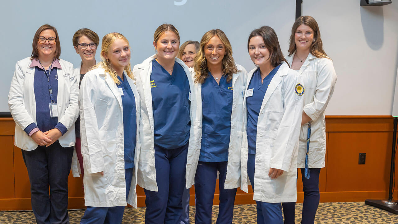 four nursing students smile in their white coats while their photo is taken
