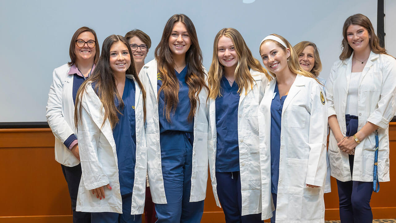 four nursing students wear their white coats and pose together for a photo