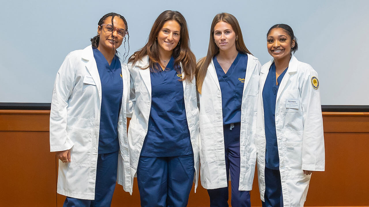 four nursing students smile in their white coats