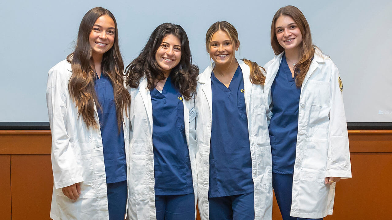 four nursing students in white coats have their photo taken