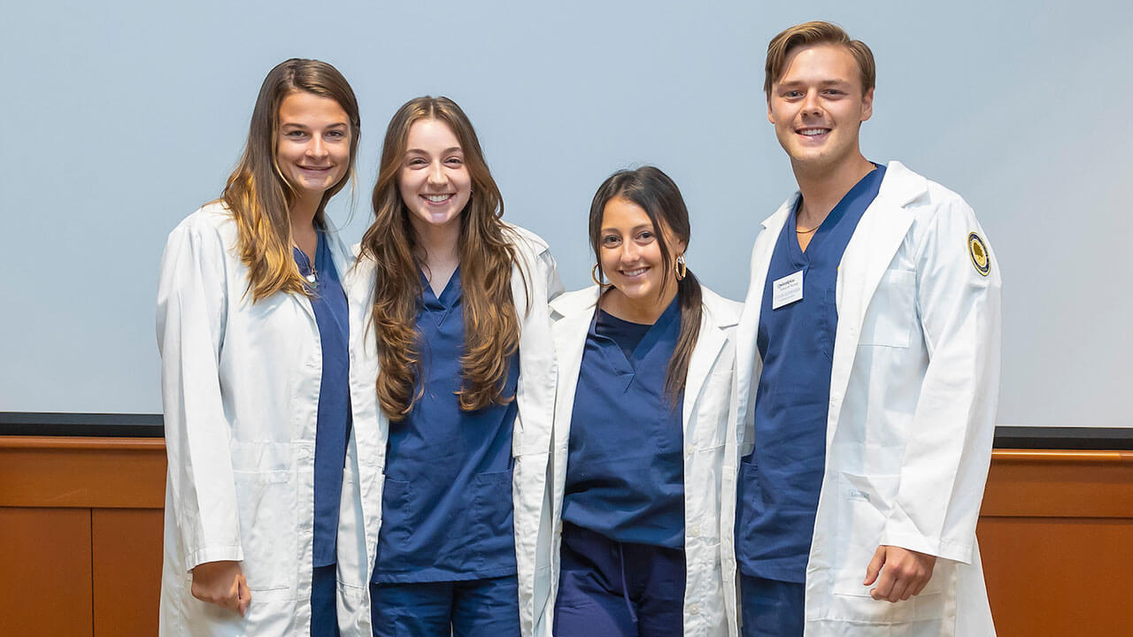 four nursing students wear their new white coats to pose for a photo