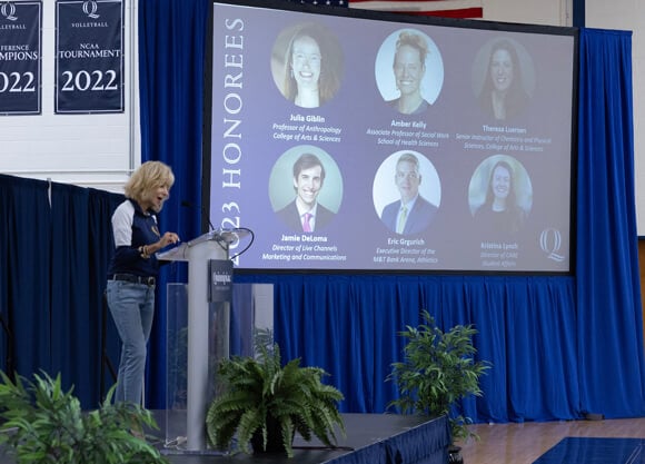 Judy Olian speaks at a podium with a screen showing the 2023 excellence honorees